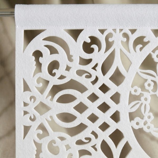 Zbliżenie na biały materiał z ażurowym, geometrycznym wzorem o precyzyjnych krawędziach.